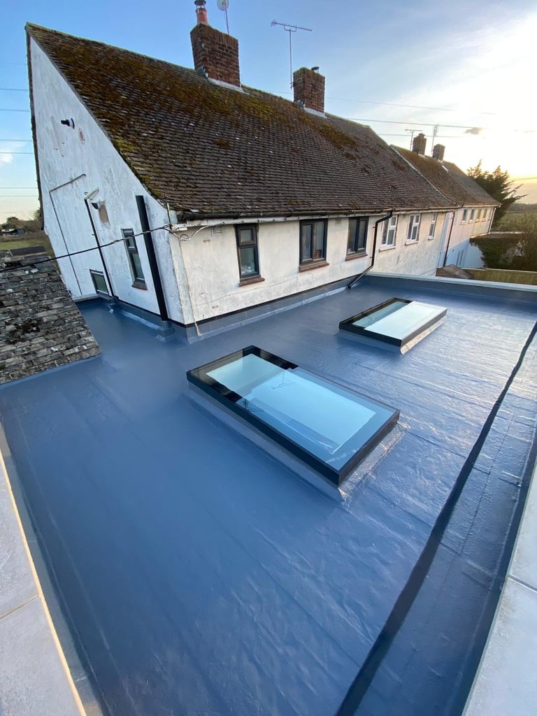 Aerial view of a white cottage with pitched roof and two skylight windows on a blue flat roof, photographed during golden hour.