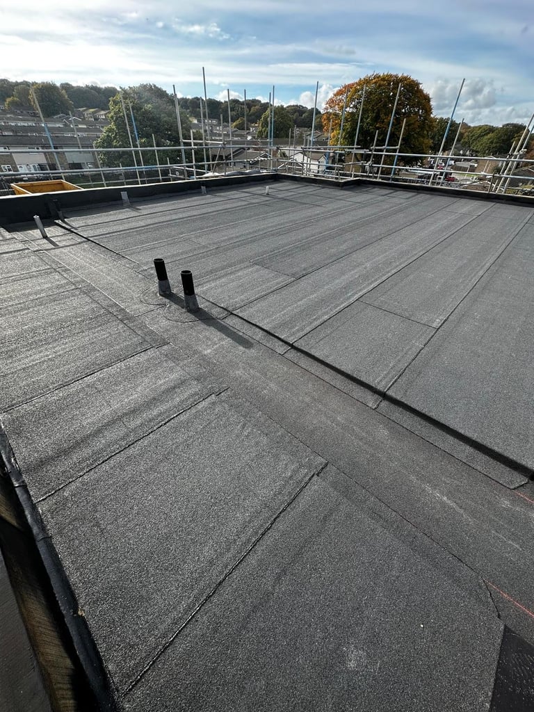 Empty rooftop with dark waterproof membrane, metal railings, and marina with sailboats visible in background