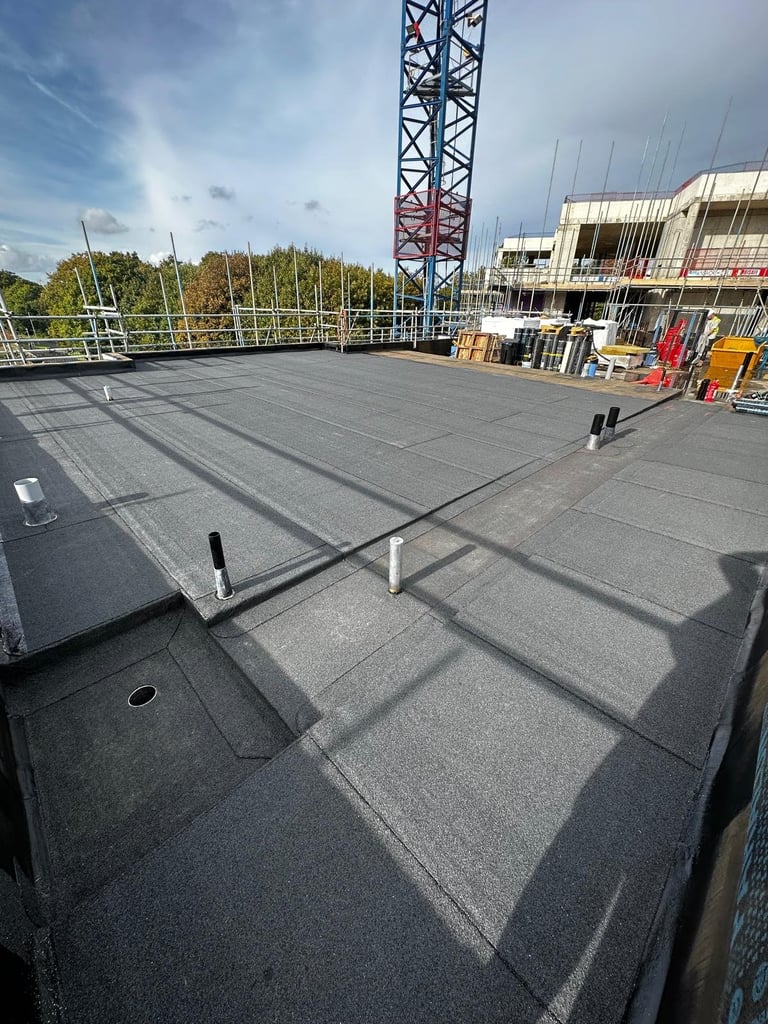 Rooftop construction area with gray membrane flooring, metal framework, red tower crane, and building under development