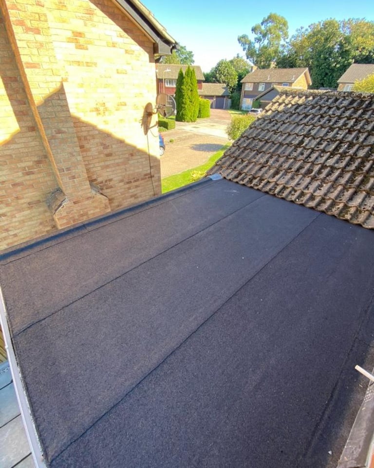 Aerial view of a newly installed black flat roof on a brick residential building with surrounding houses and green trees